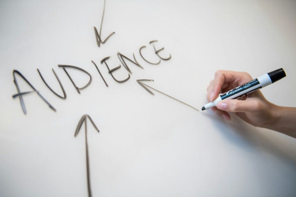 Woman's handwriting the word "audience" on a whiteboard, with arrows pointing to it.